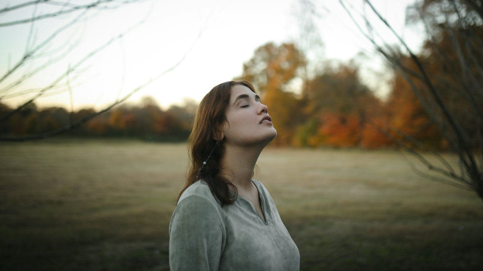 A woman standing in an autumn field with her eyes closed, breathing slowly