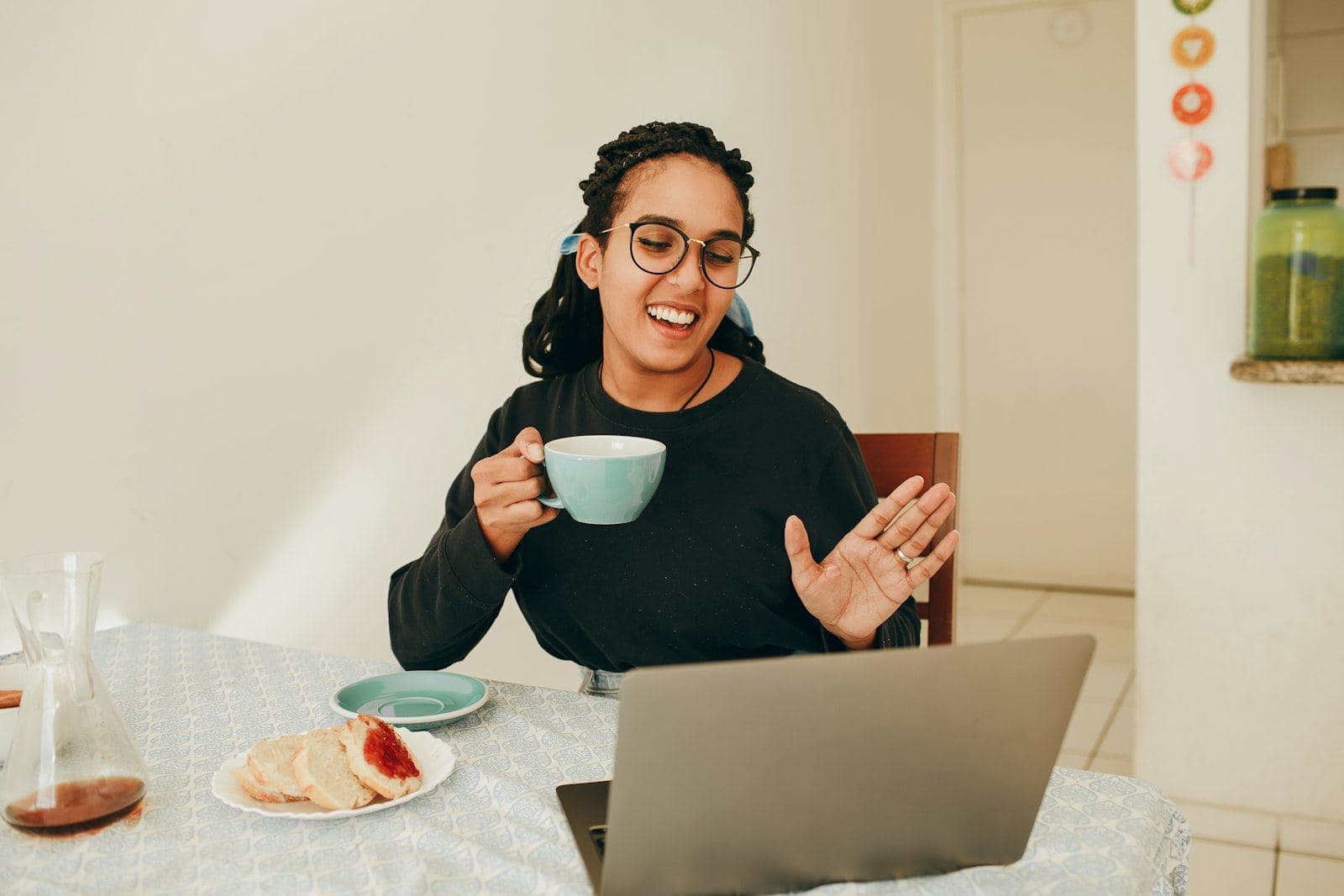 A woman holding a mug and talking to someone on her laptop at home