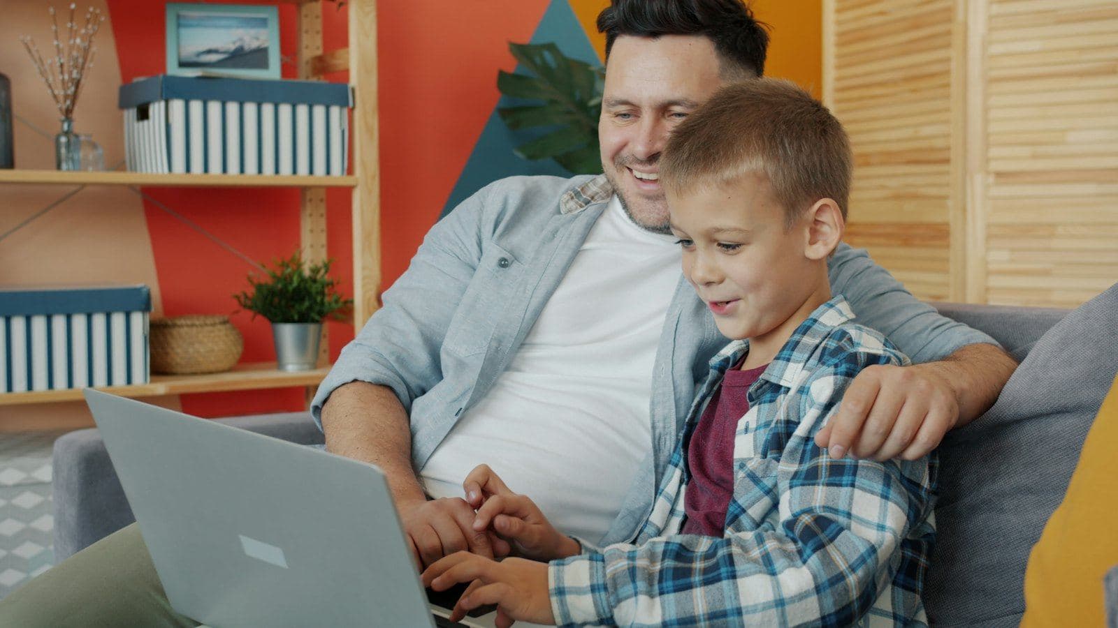 A father and son sitting together on a sofa looking at a laptop