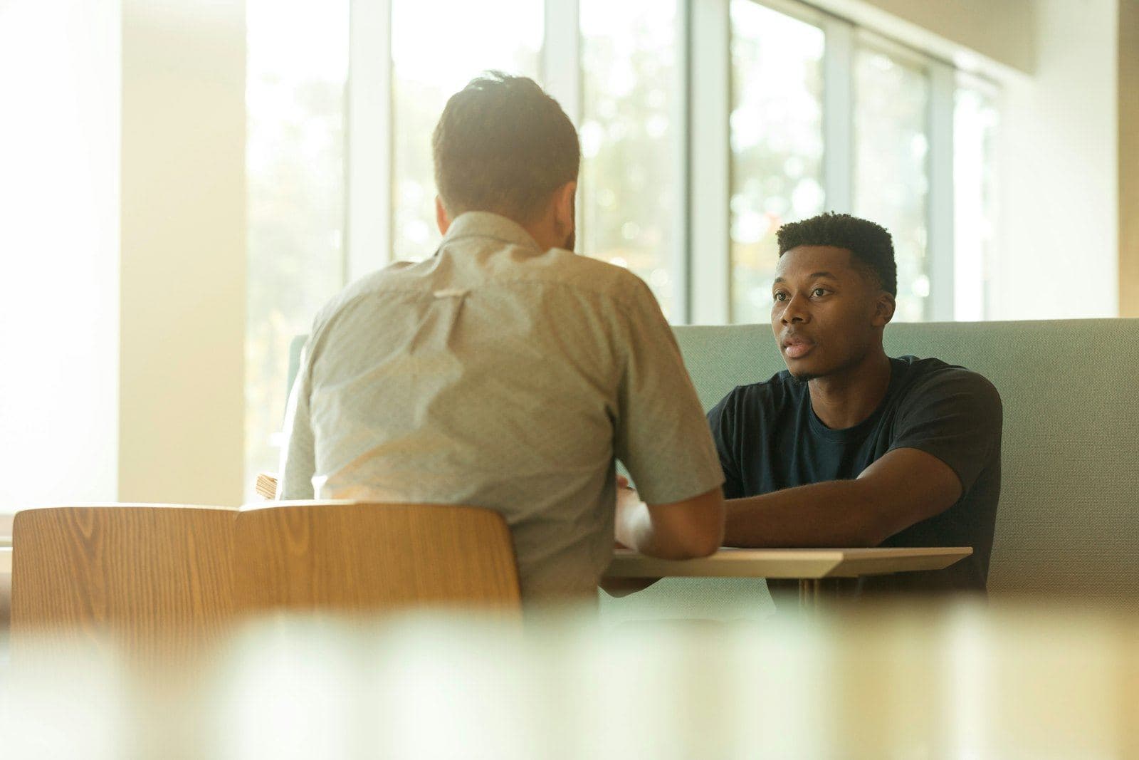 Two men talking across a table in a bright room