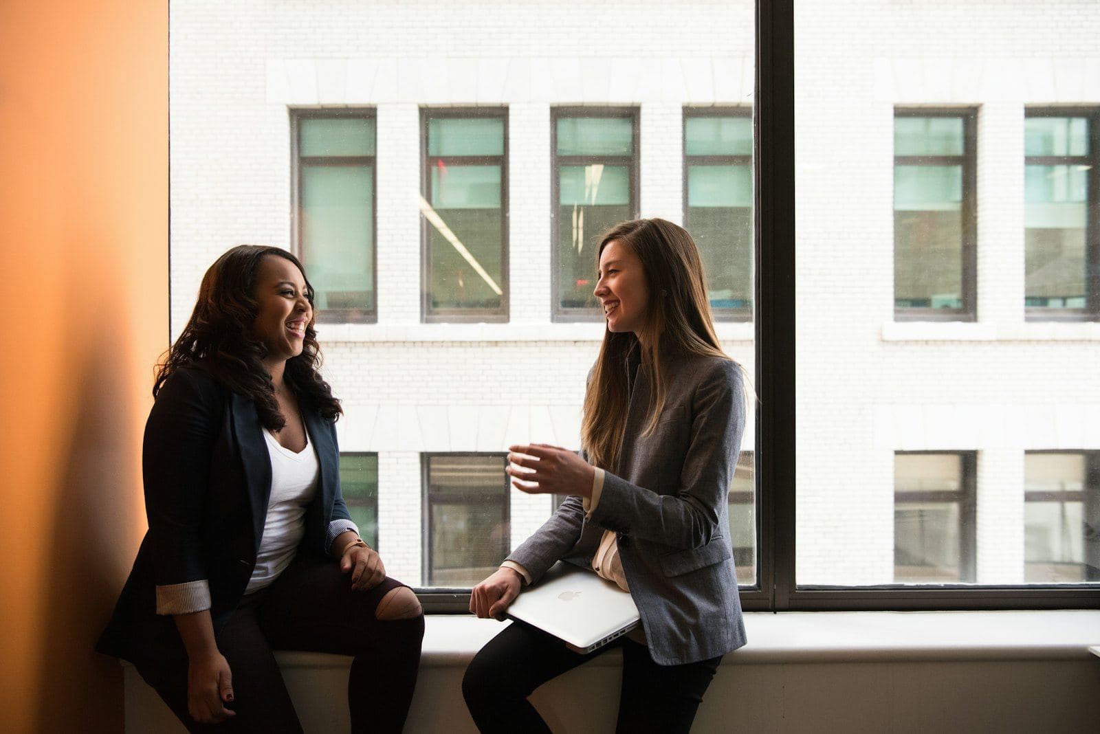 Two women laughing together by a window