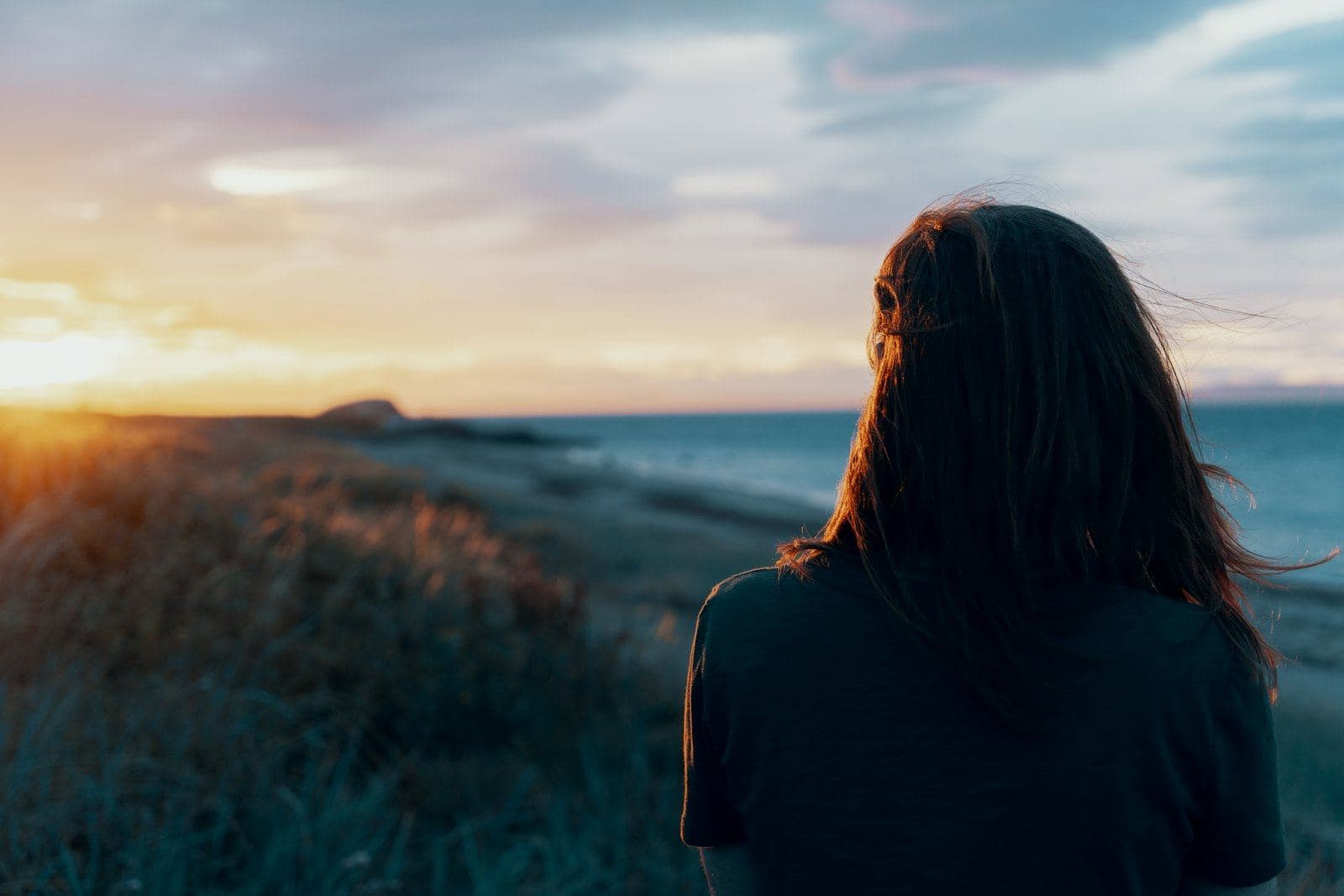 A woman looking out over calm water at sunset