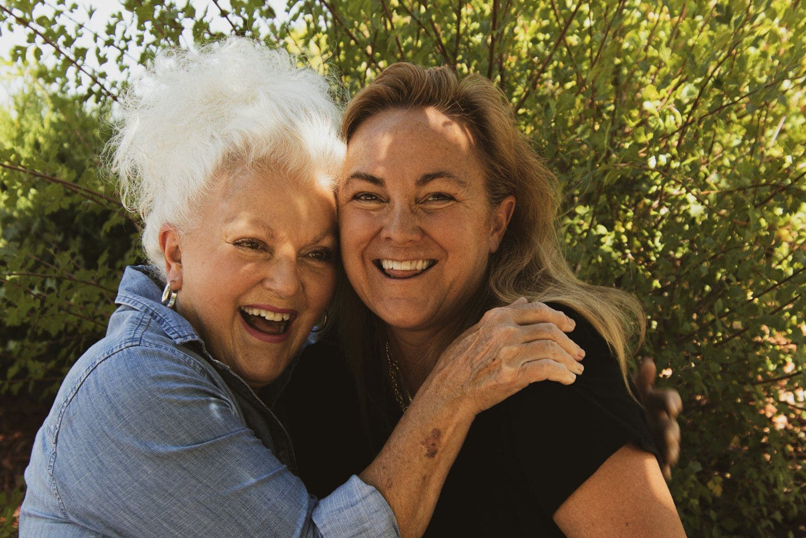 An older mother and her adult daughter sharing a hug outdoors
