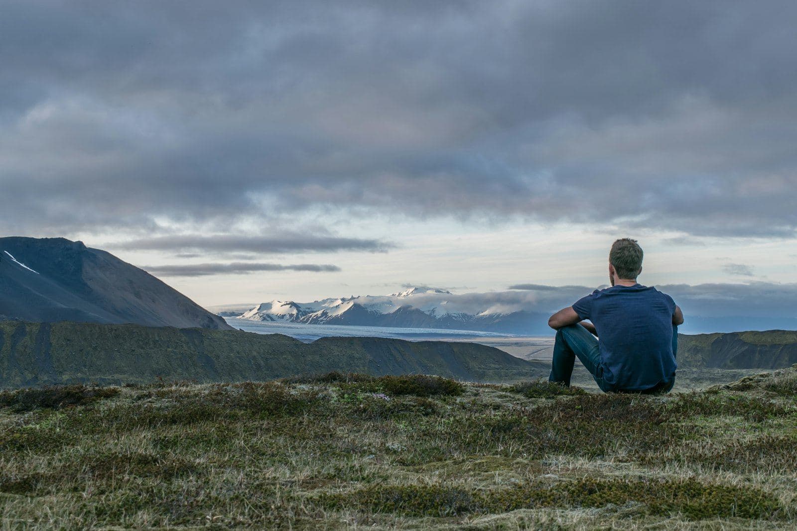 A man sitting alone on a hillside looking out at the mountains