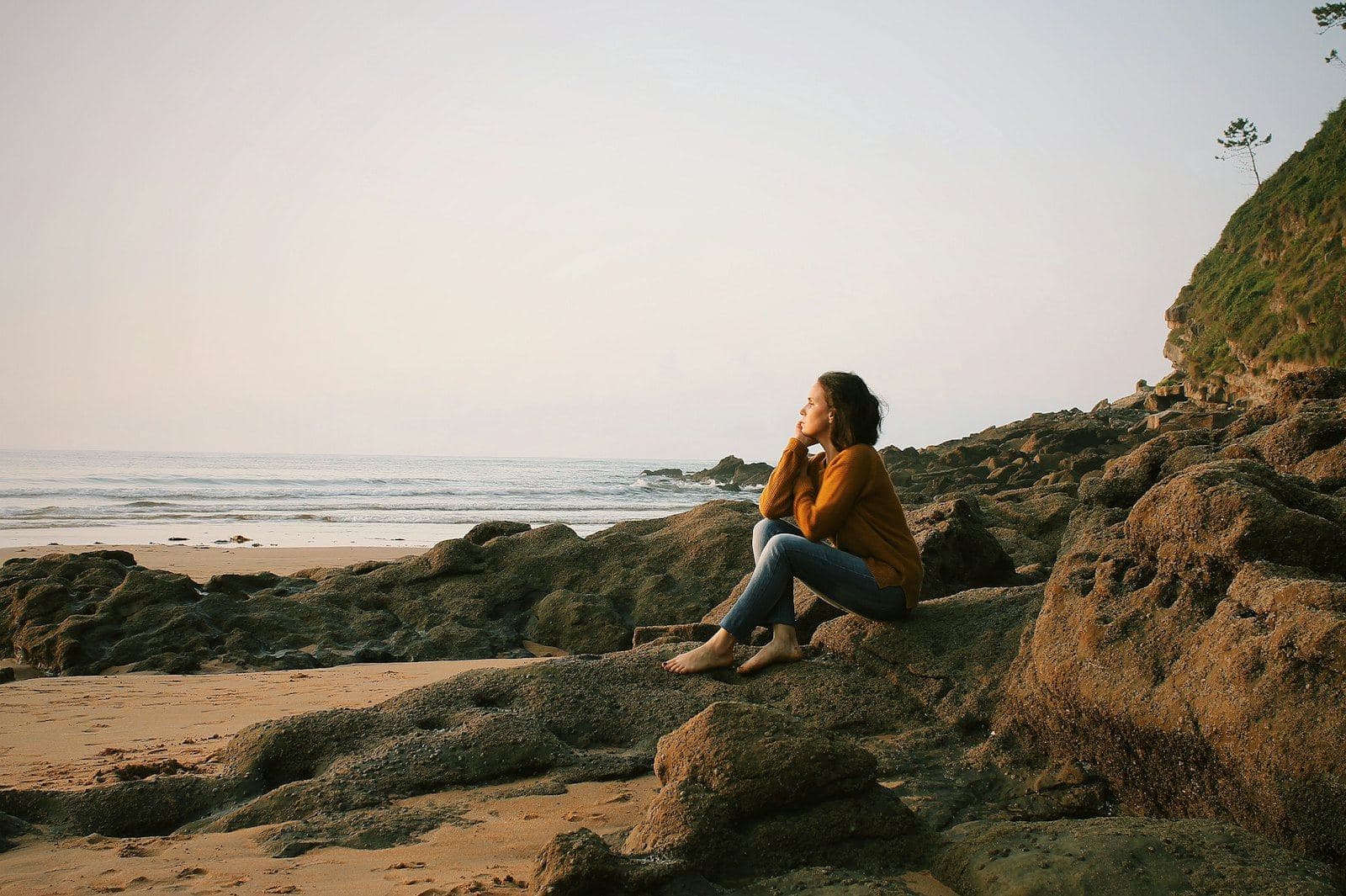 A woman sitting on rocks by the sea, lost in thought