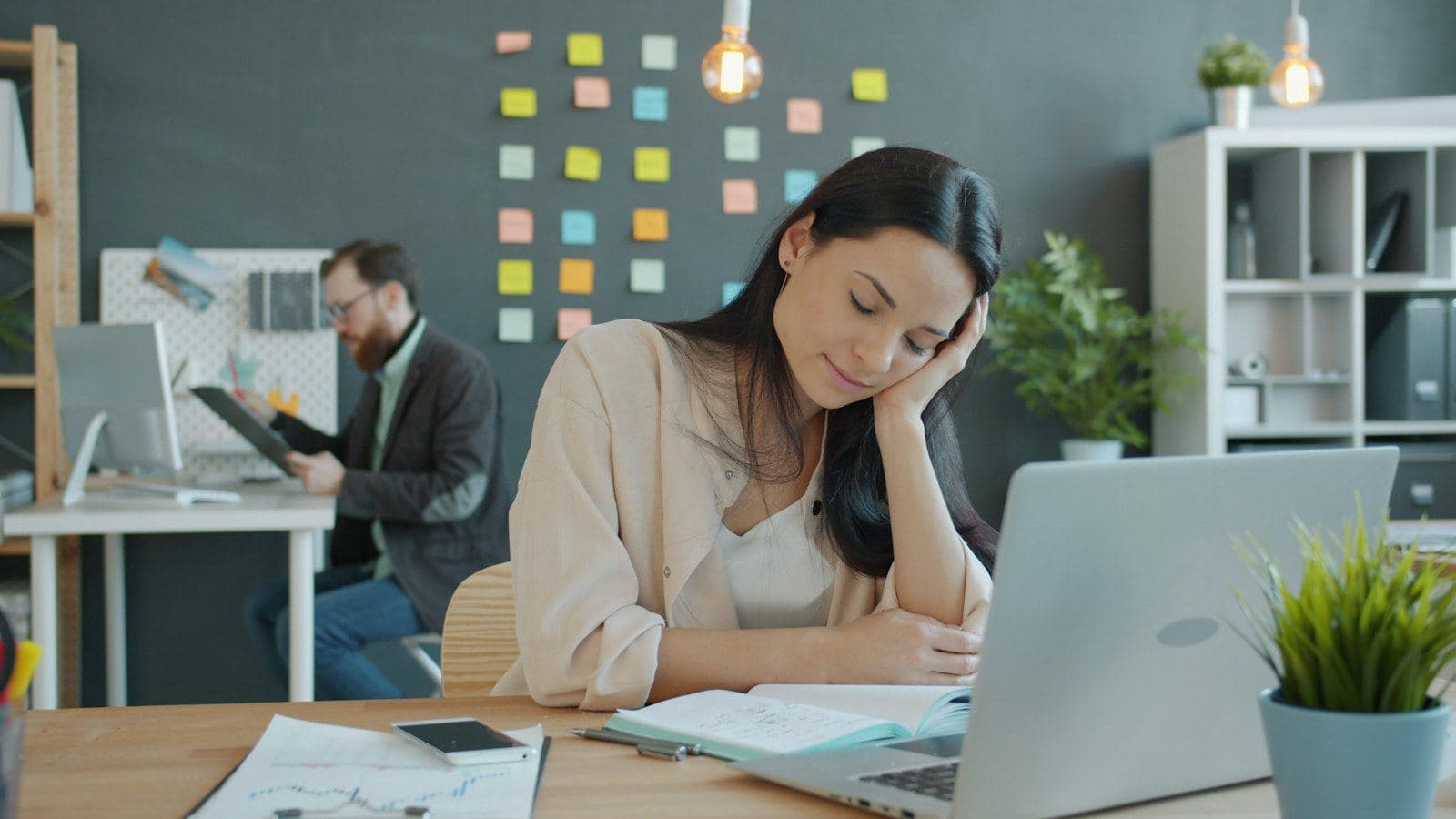 A woman at a desk pausing to think in a bright office