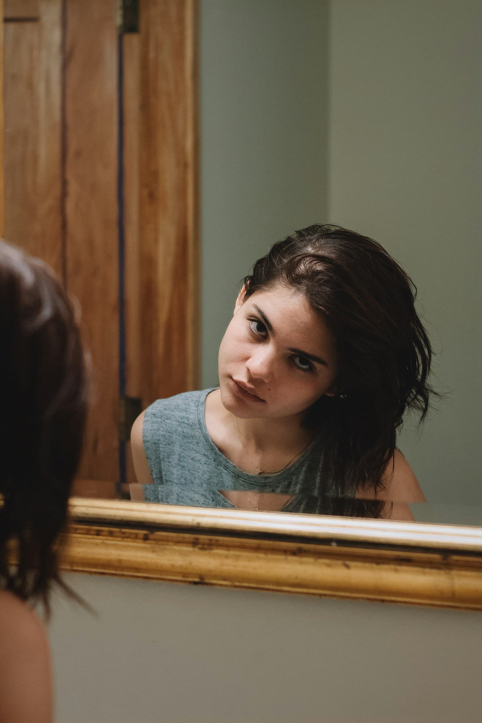 A young woman looking at her reflection in a gold-framed mirror