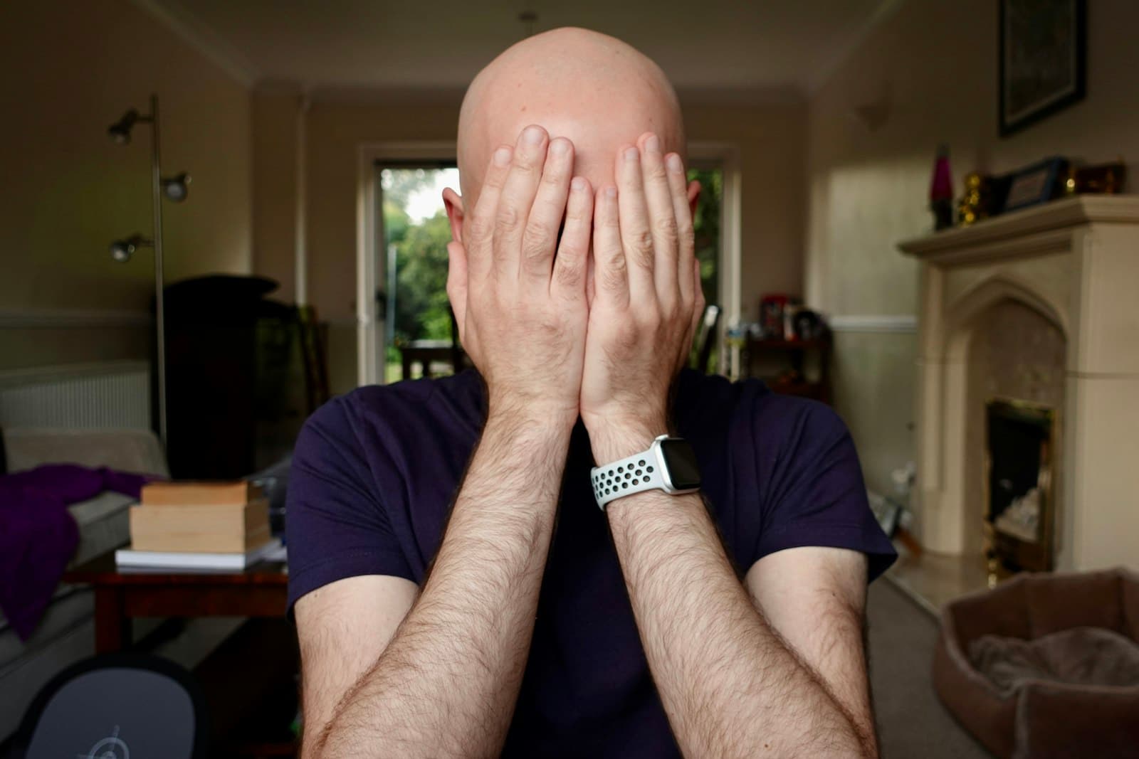 A bald man at home covering his face with both hands