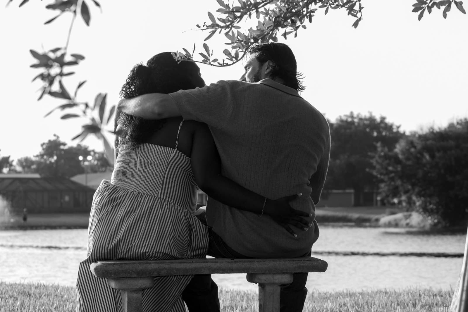 A couple sitting on a bench by a lake with their arms around each other, in black and white
