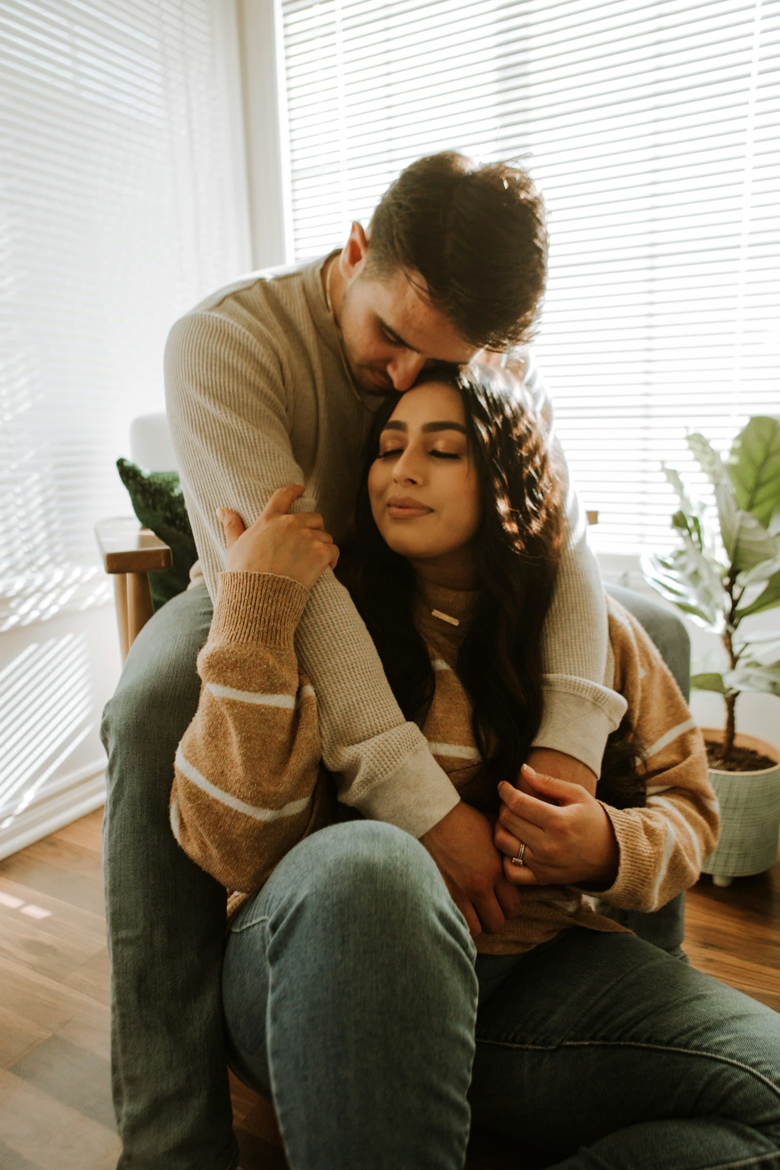 A man holding his partner close as she rests against him in a sunlit room