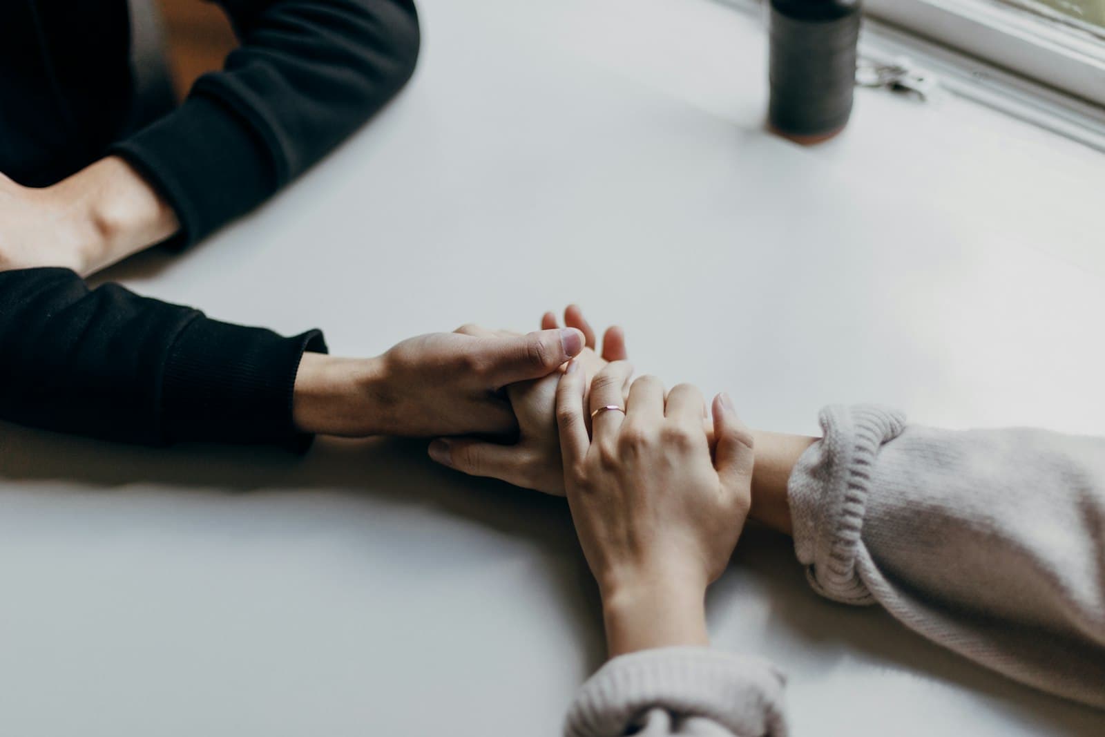 Two people reaching across a white table to hold hands beside a coffee cup
