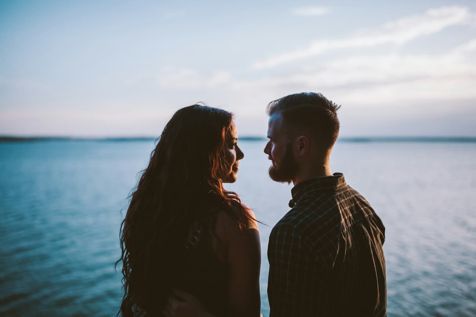 A man and a woman facing each other by a lake, talking calmly