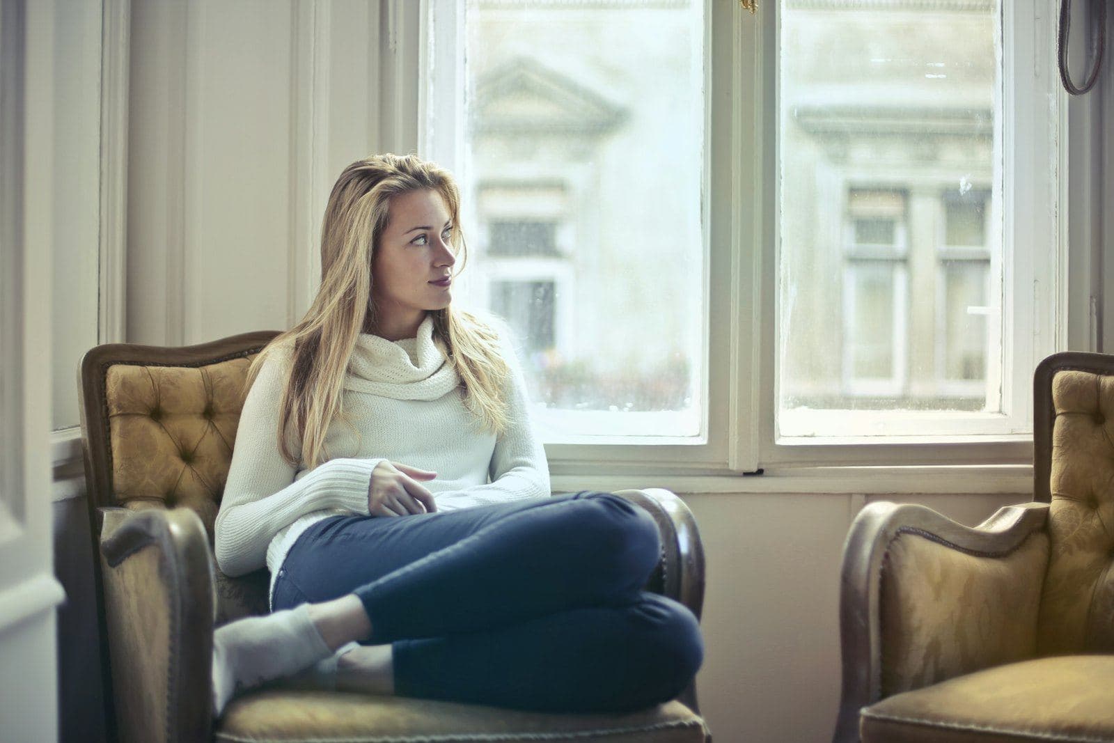 A woman sitting in an armchair by a window, reflecting