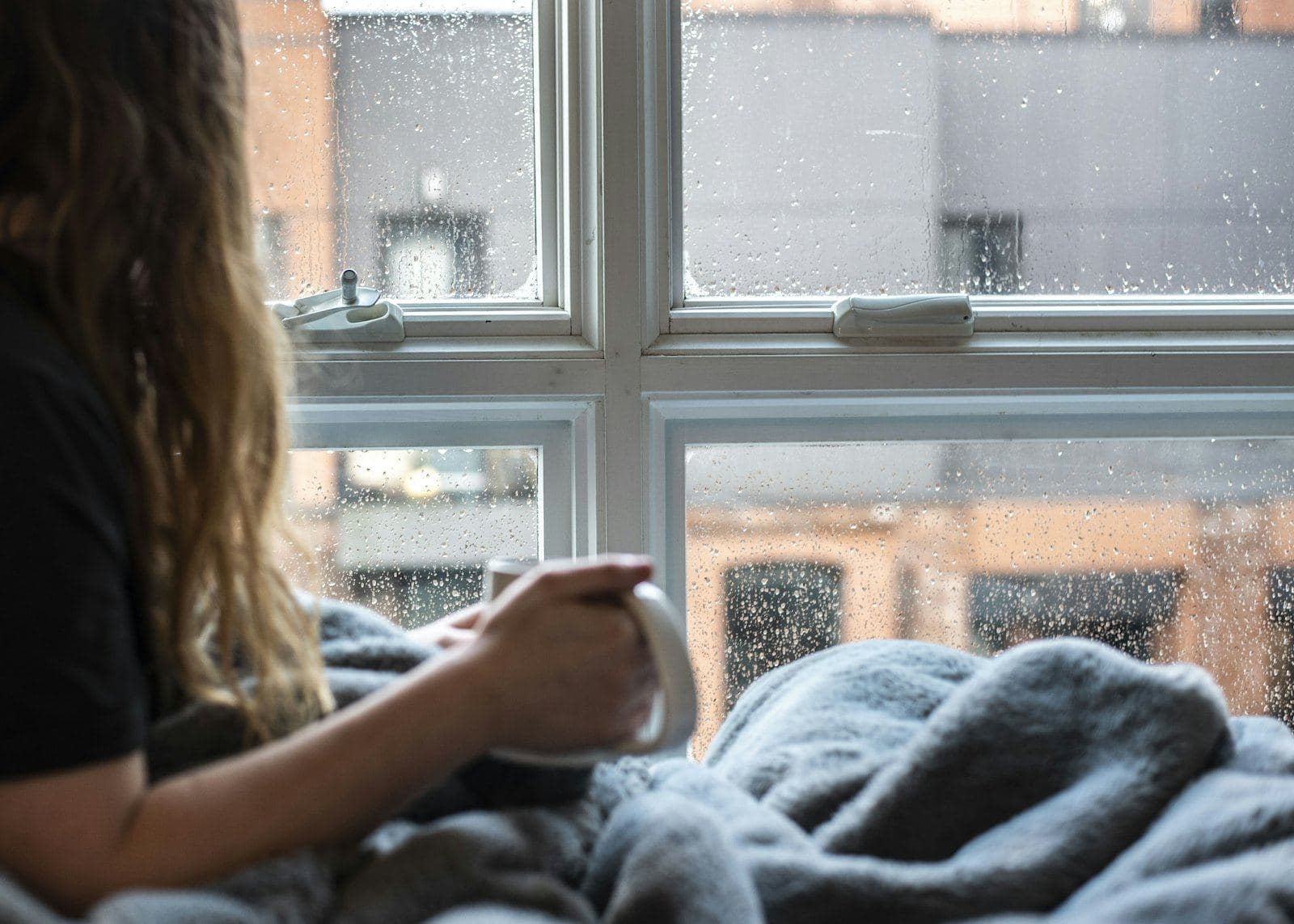 Someone wrapped in a blanket by a rainy window