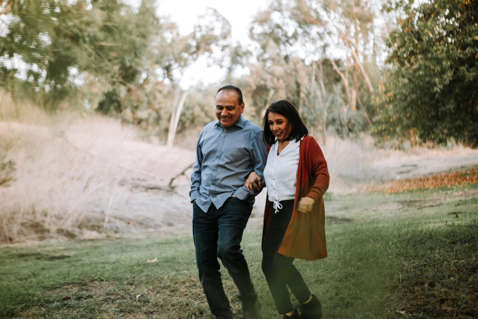 A middle-aged couple laughing together as they walk through a grassy field