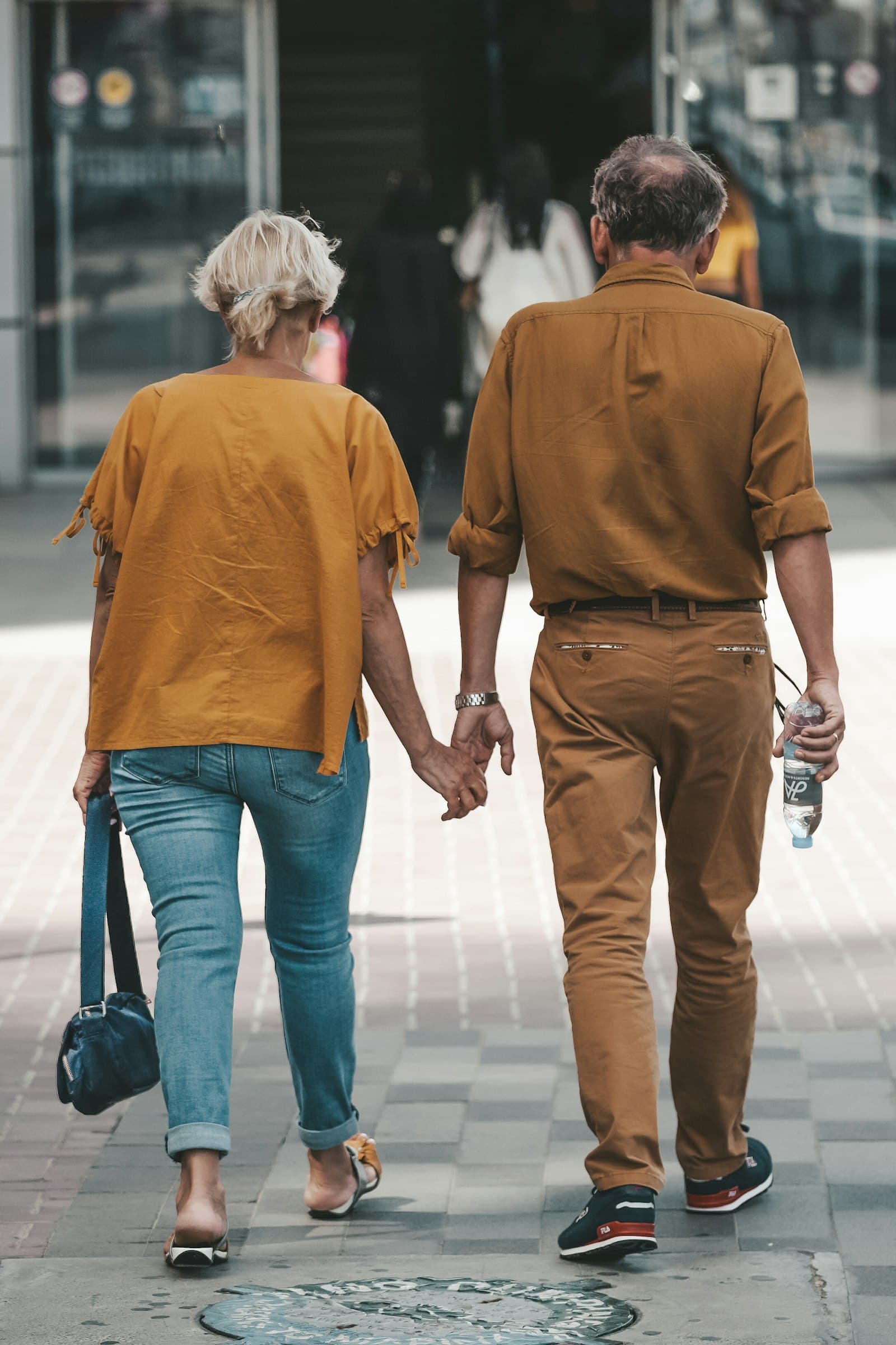 A couple seen from behind holding hands as they walk along a city street