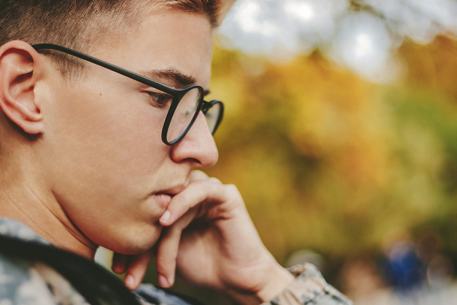 A young man in glasses resting his chin on his hand, looking down in thought