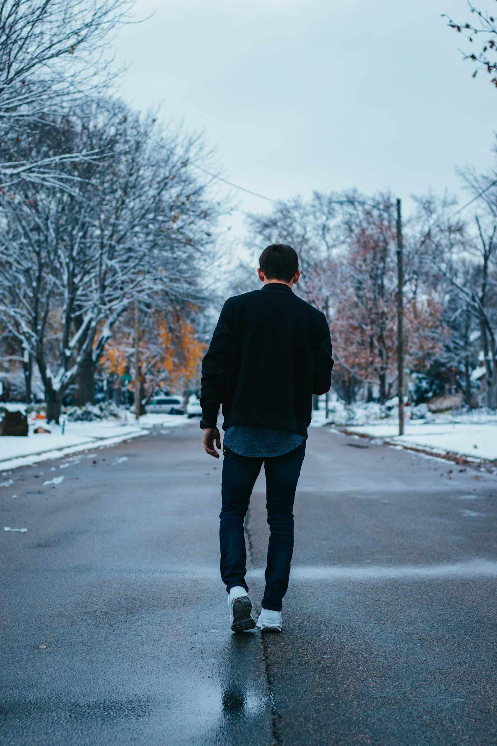 A man in a dark coat walking alone down the middle of a quiet snowy street