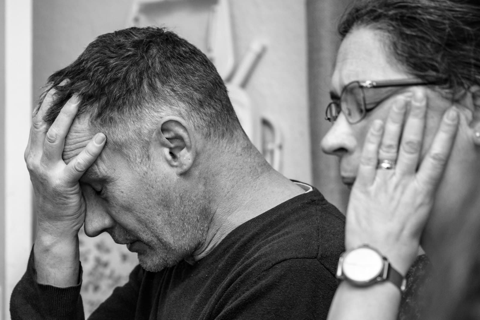 A middle-aged man with his hand on his forehead beside a woman touching her face, in black and white
