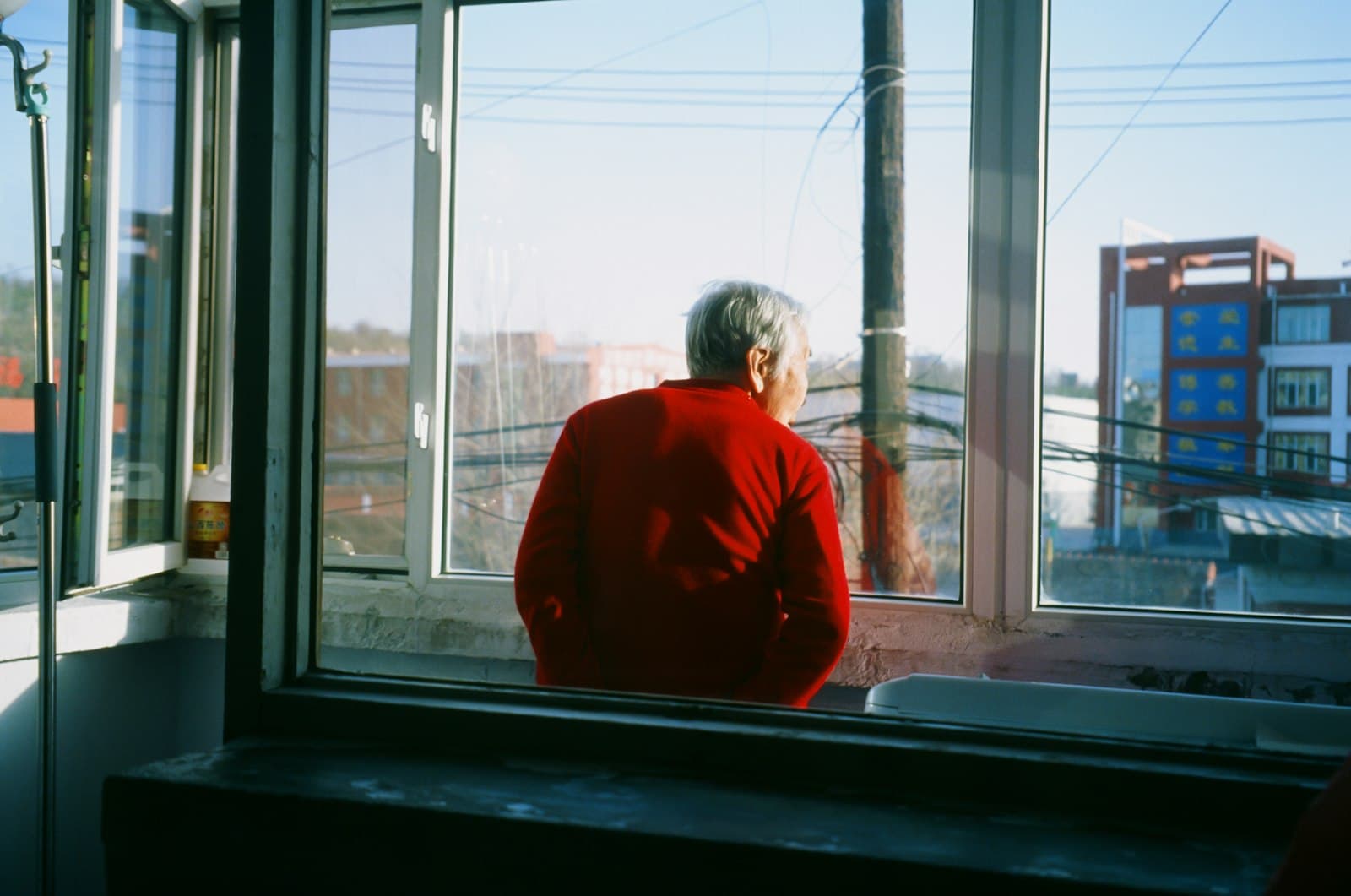 An older man in a red sweater looking out a window over the city