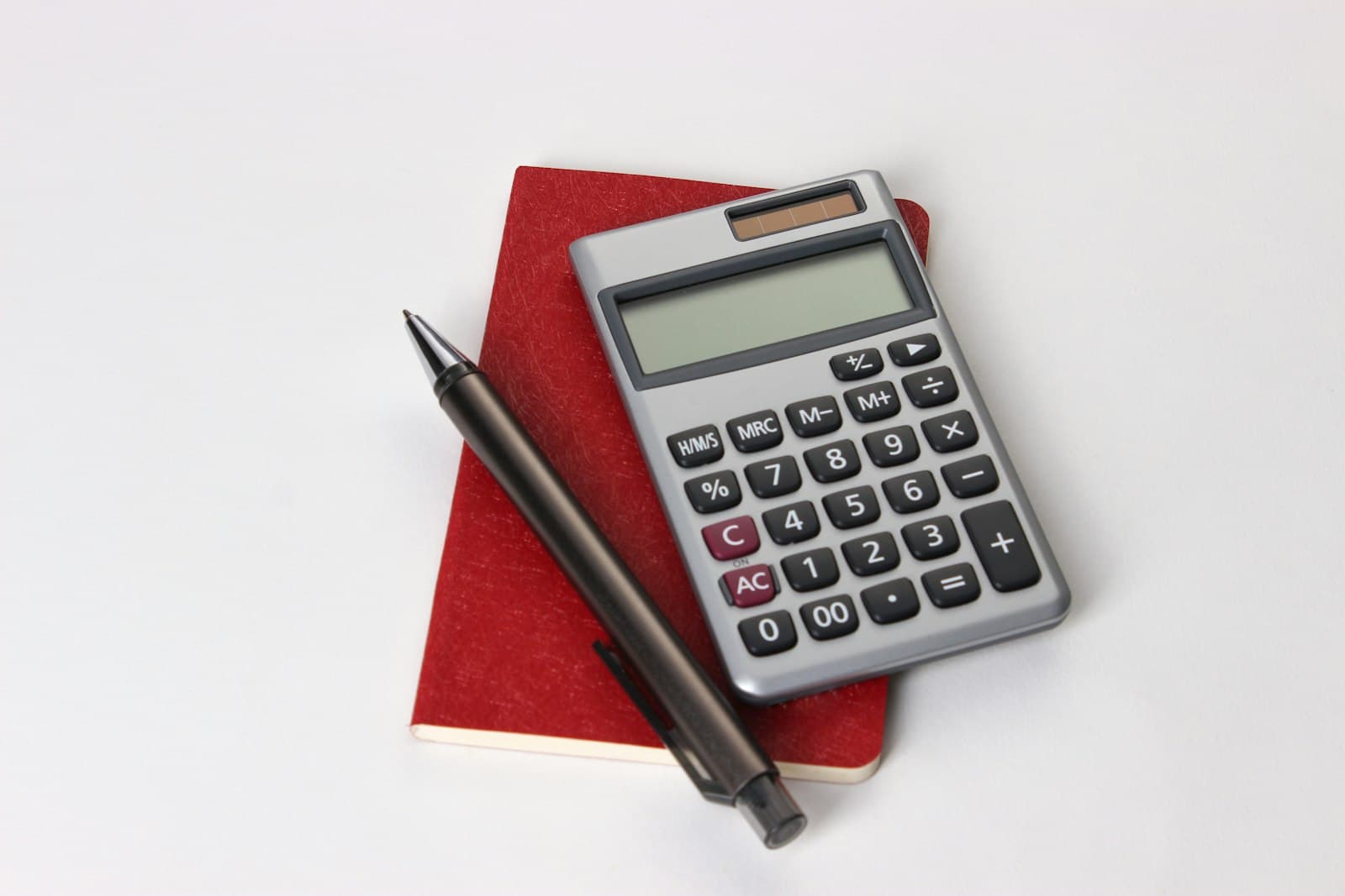 A calculator and pen on a red notebook