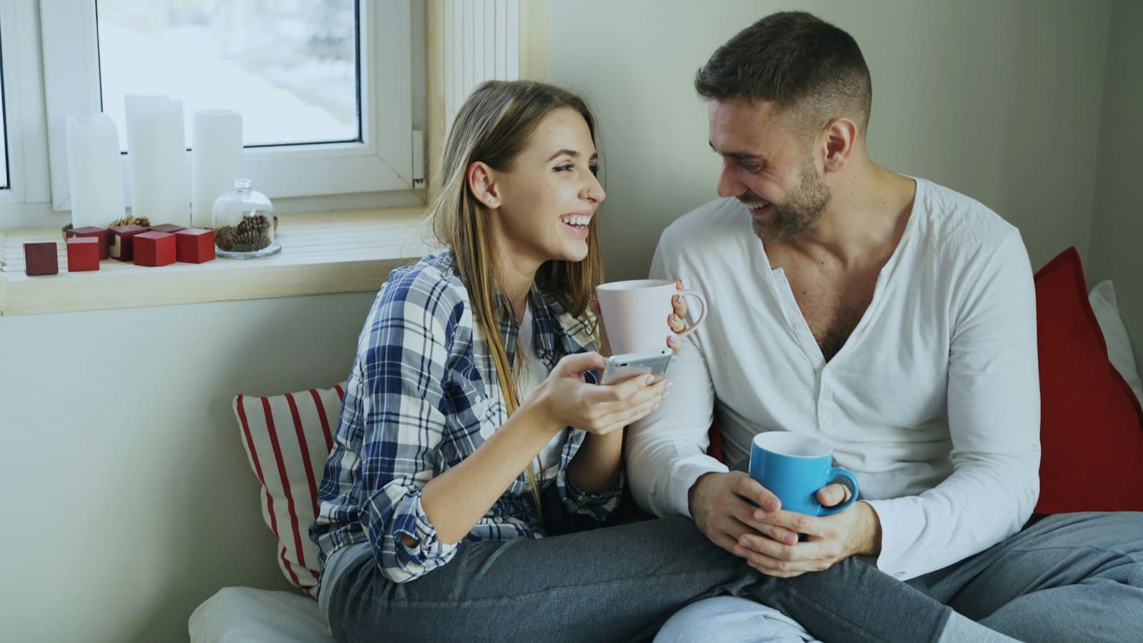 A couple sitting on a sofa holding mugs, smiling as they talk