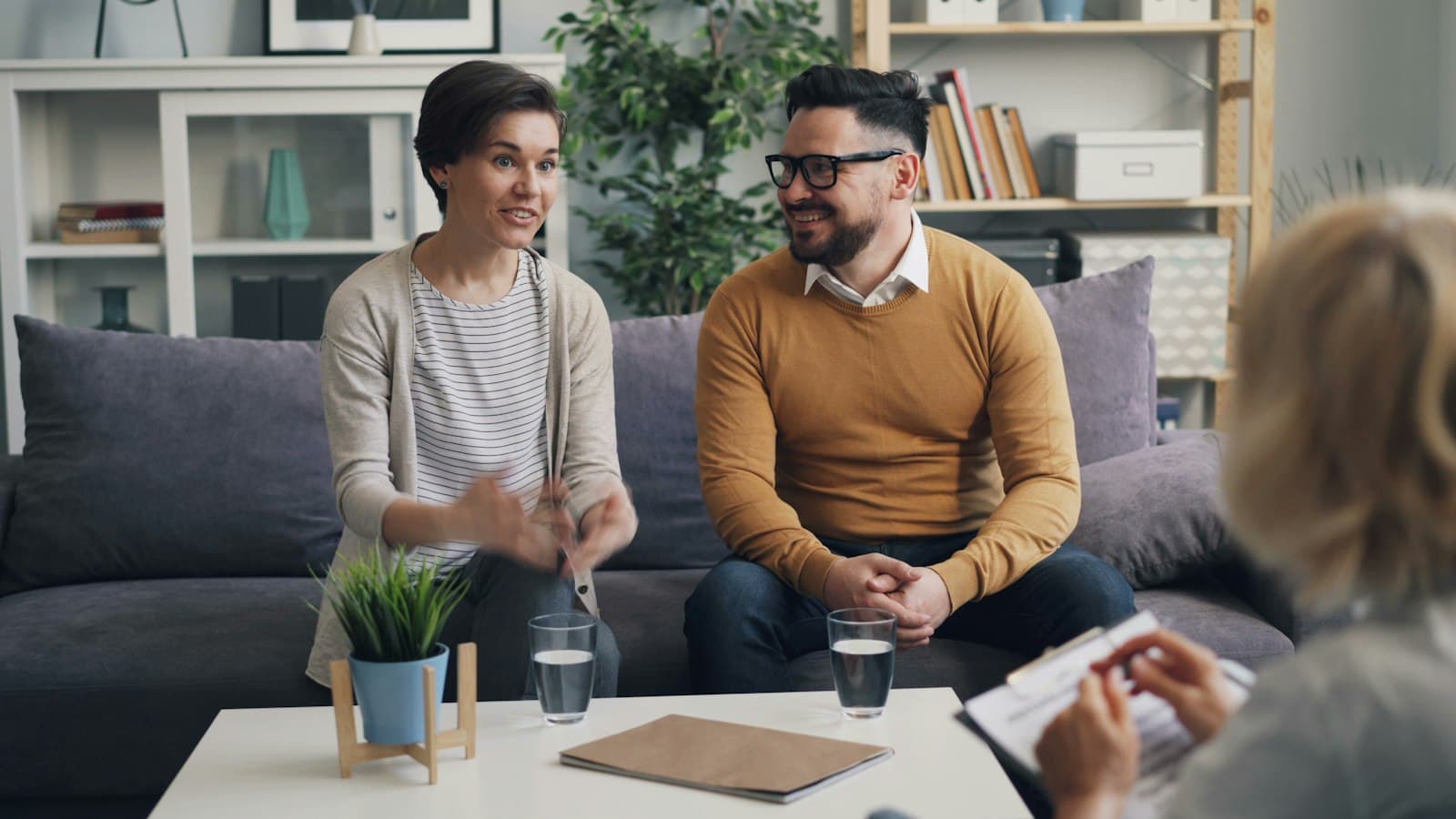 A couple sitting together on a sofa talking with a therapist who takes notes