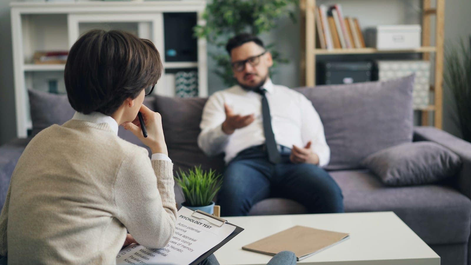 A man in a shirt and tie talking with a therapist in a bright office
