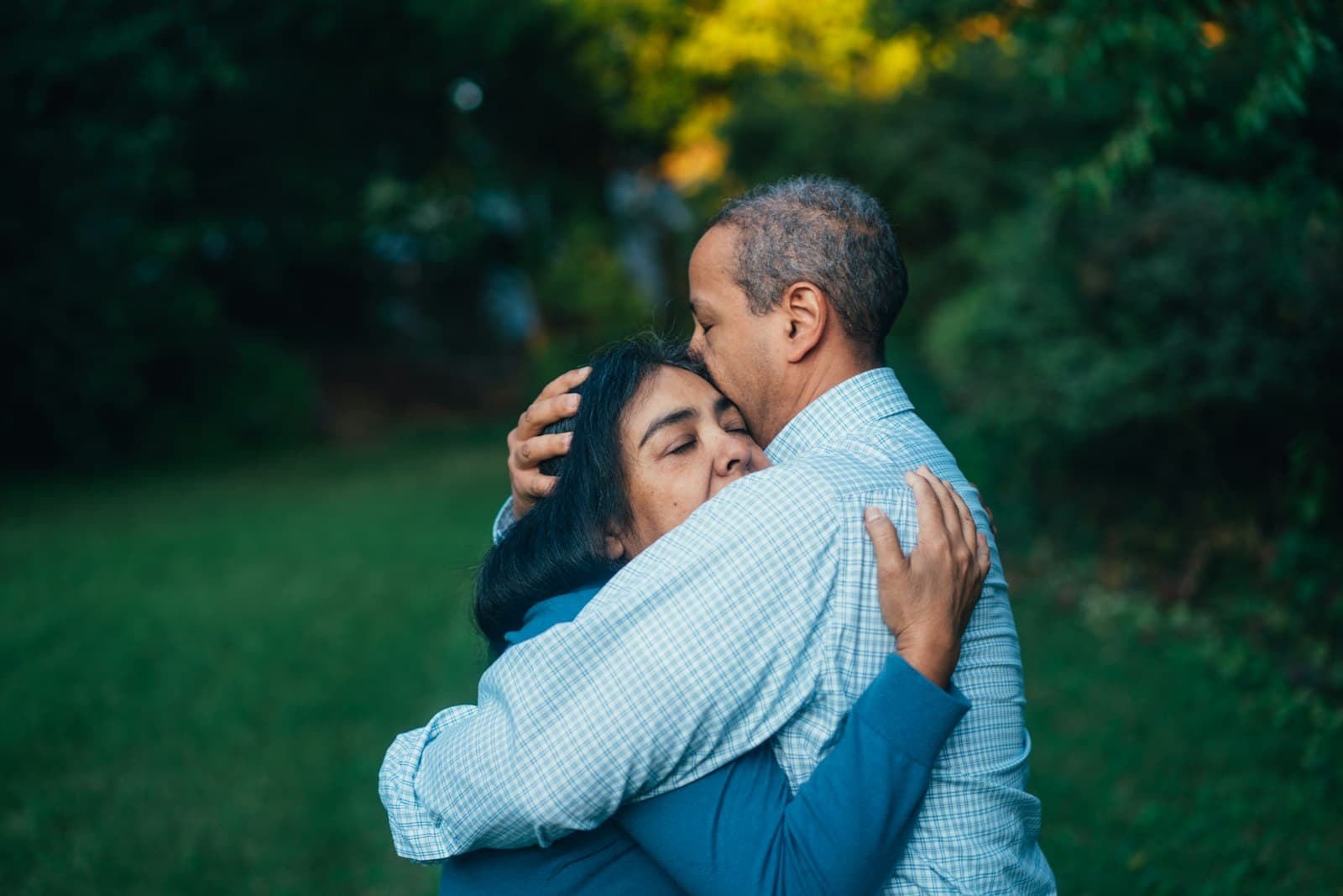 A man kissing his partner's forehead as they embrace outdoors