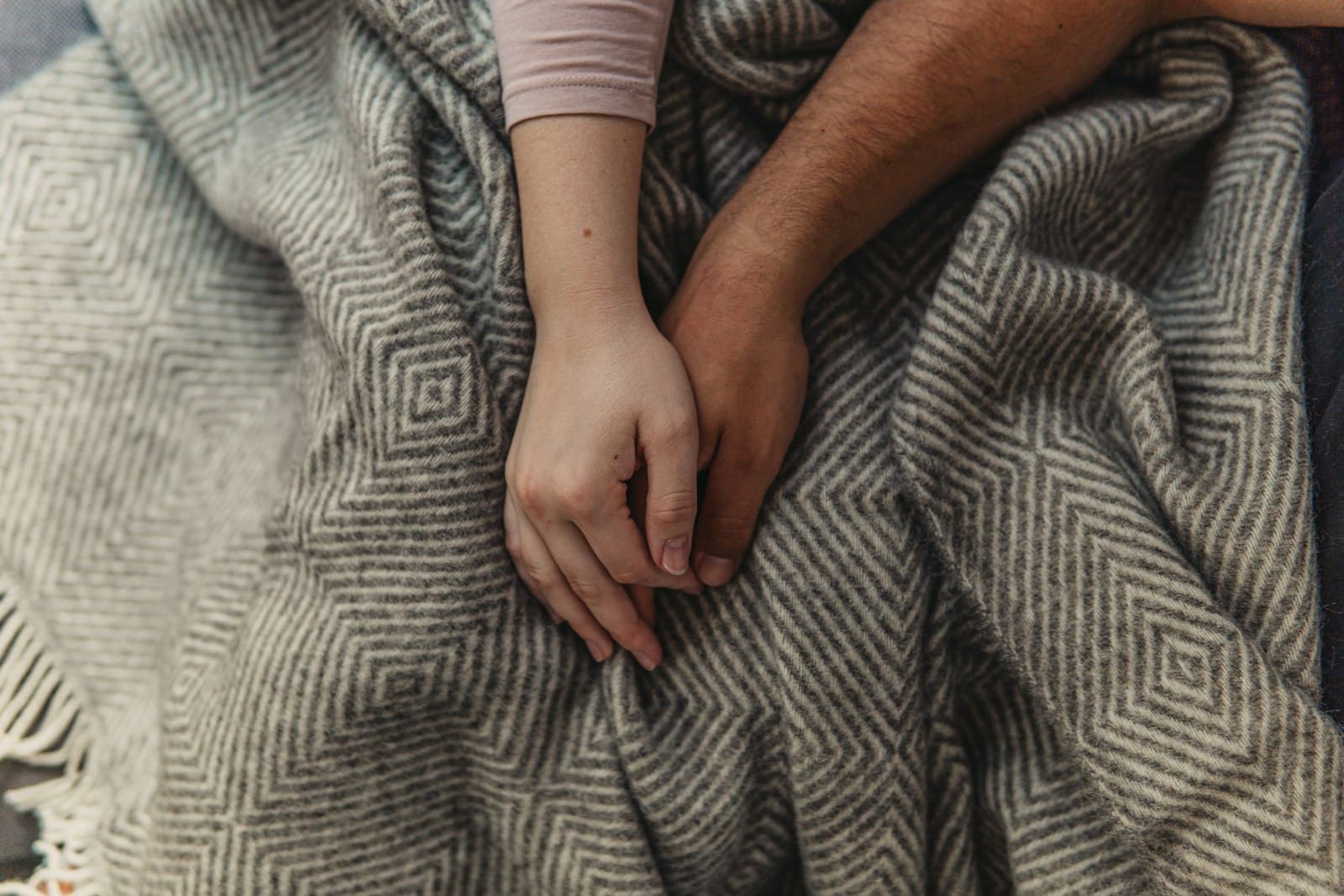 Two people holding hands on a woven blanket