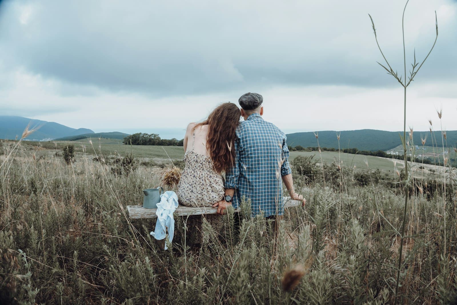A couple sitting on a bench in a grassy field with their small child, seen from behind