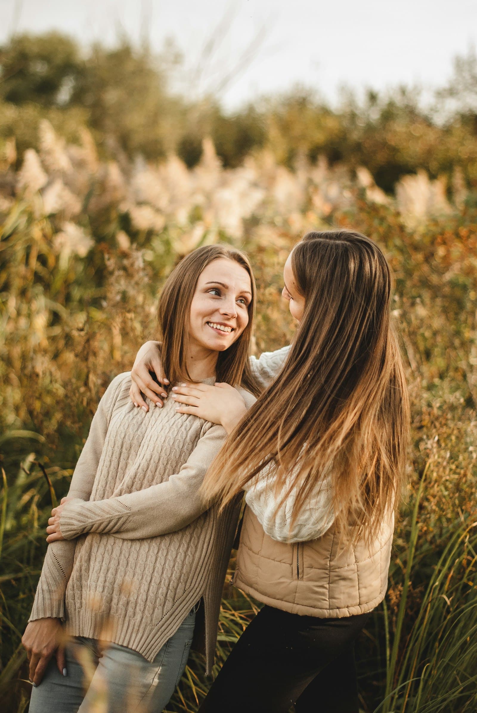 Two women standing close with arms around each other in a field of tall grass