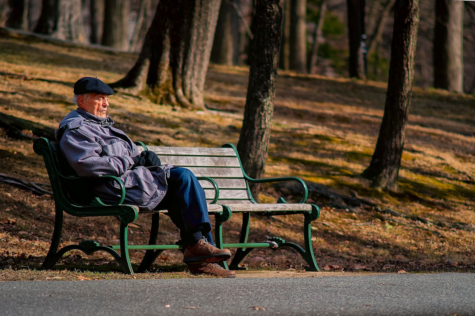 An older man in a cap and coat sitting alone on a park bench
