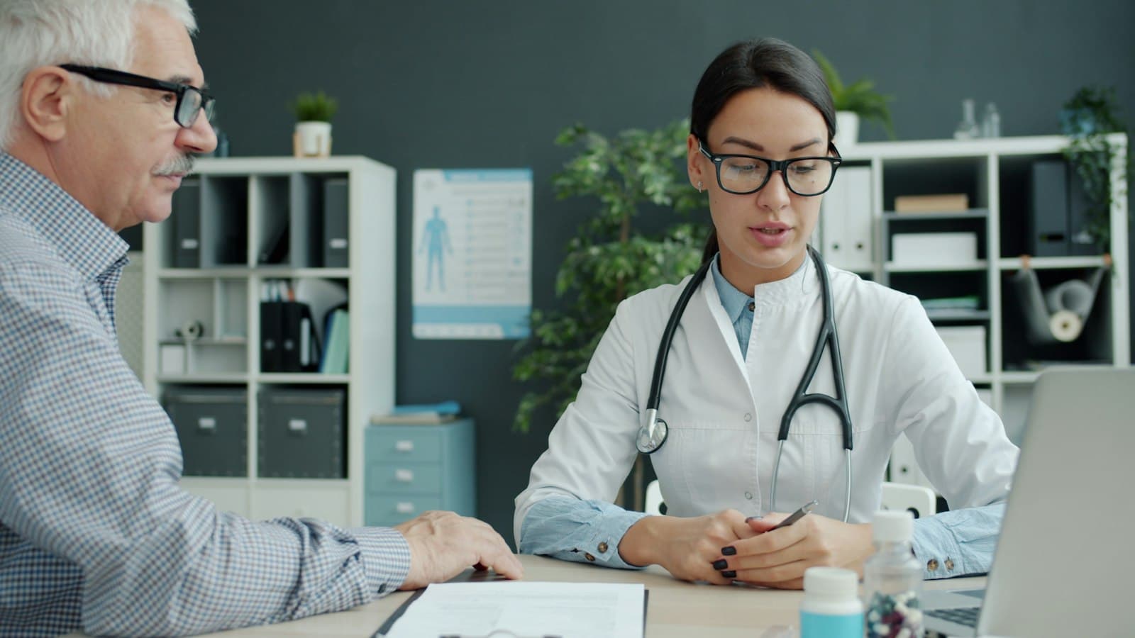 A doctor in glasses talking with an older man across her desk