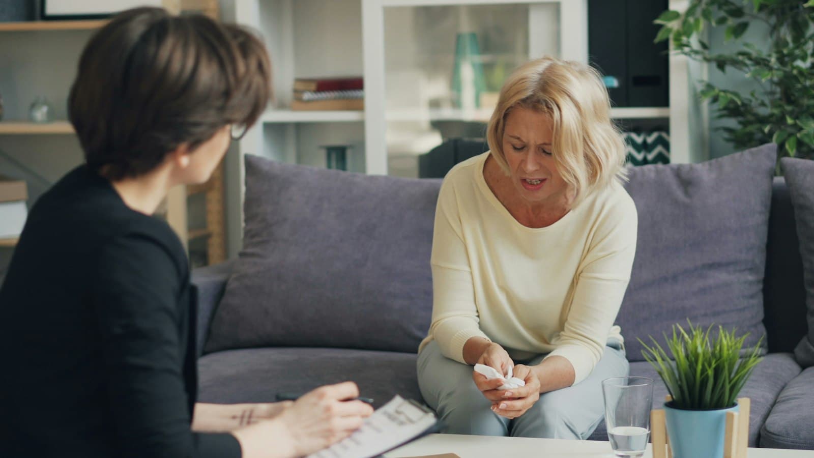 A woman on a grey sofa talking with a counselor who takes notes on a clipboard