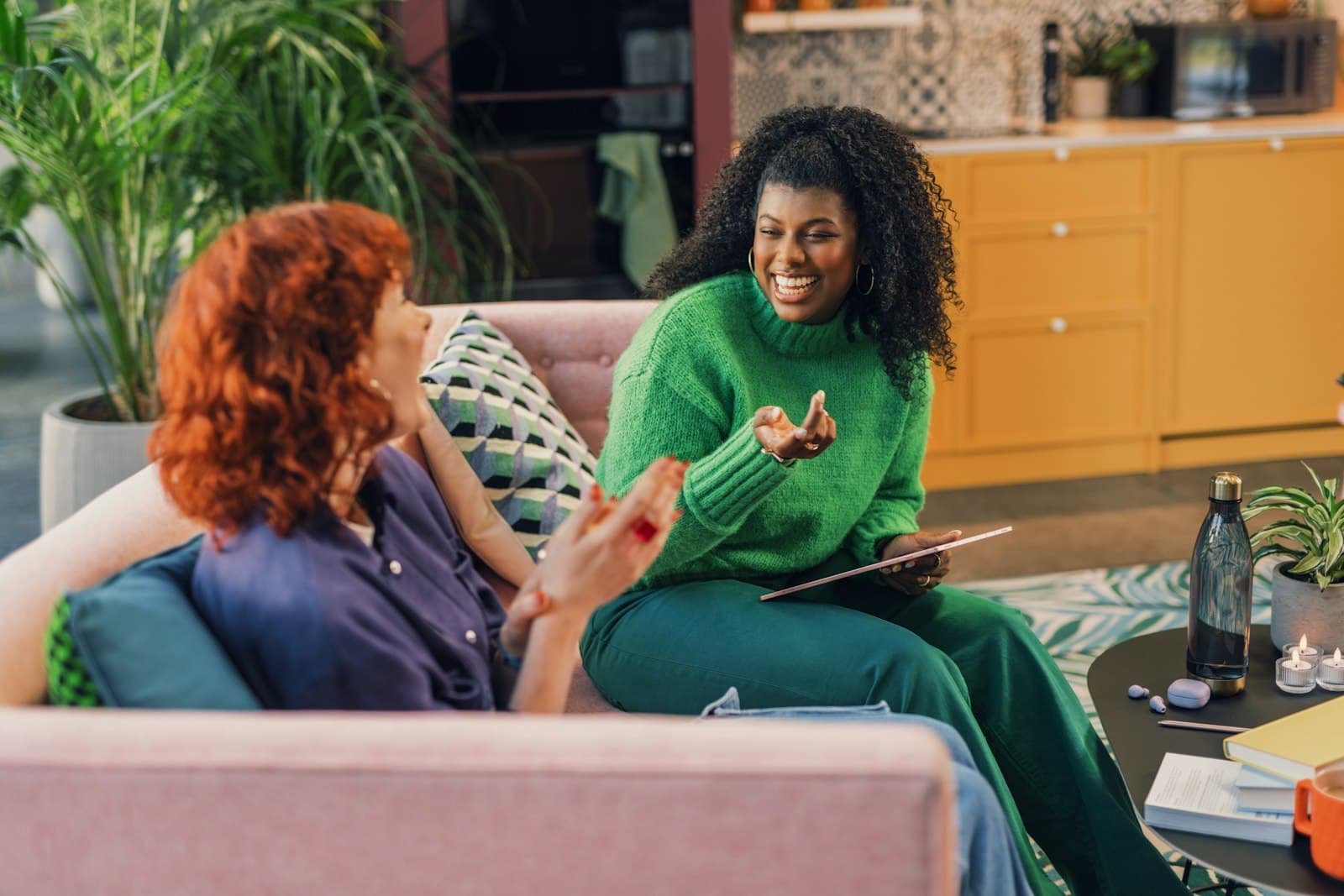 Two women sitting on a pink sofa in a sunny room, talking warmly