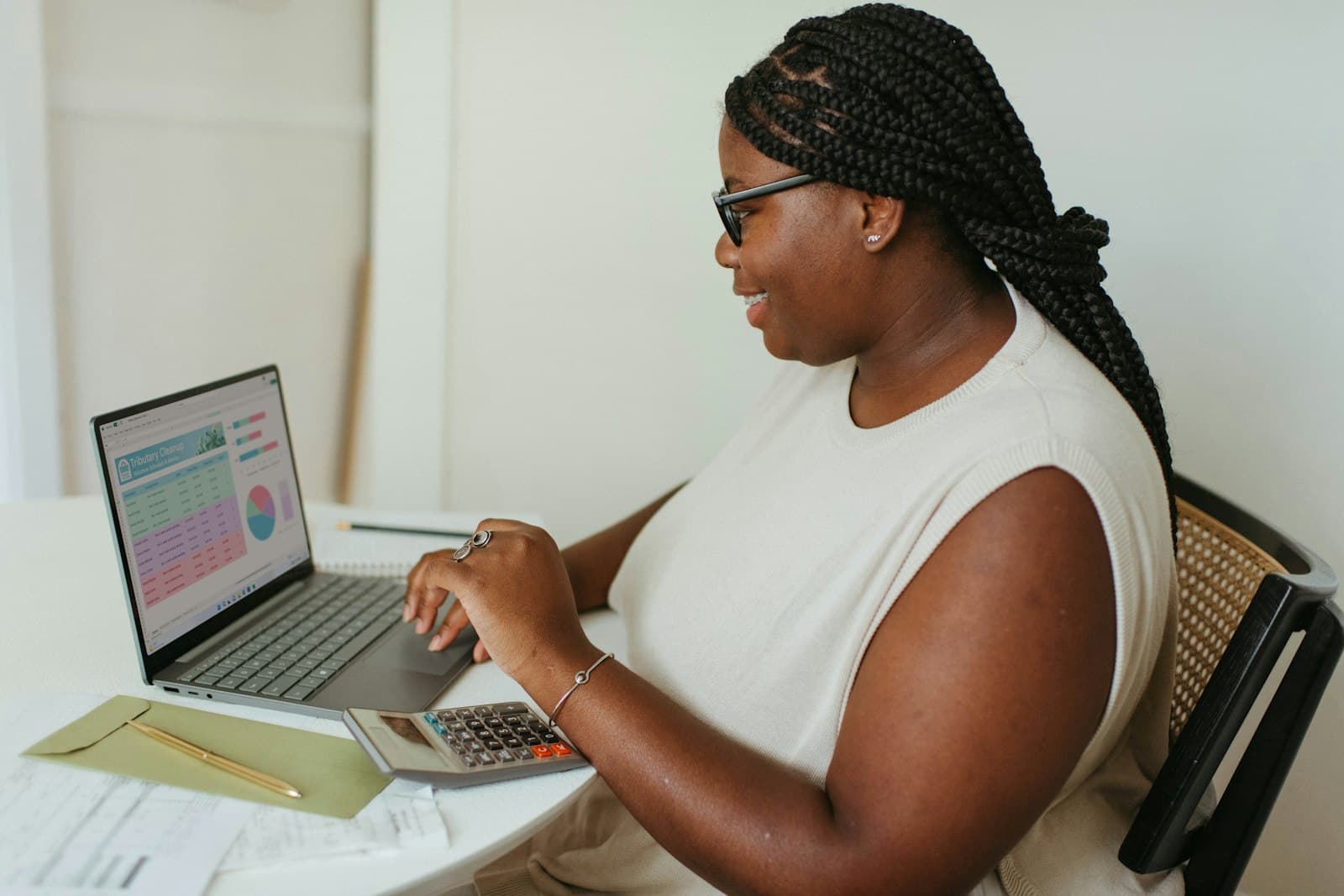 A woman at a laptop with a calculator and paperwork beside her