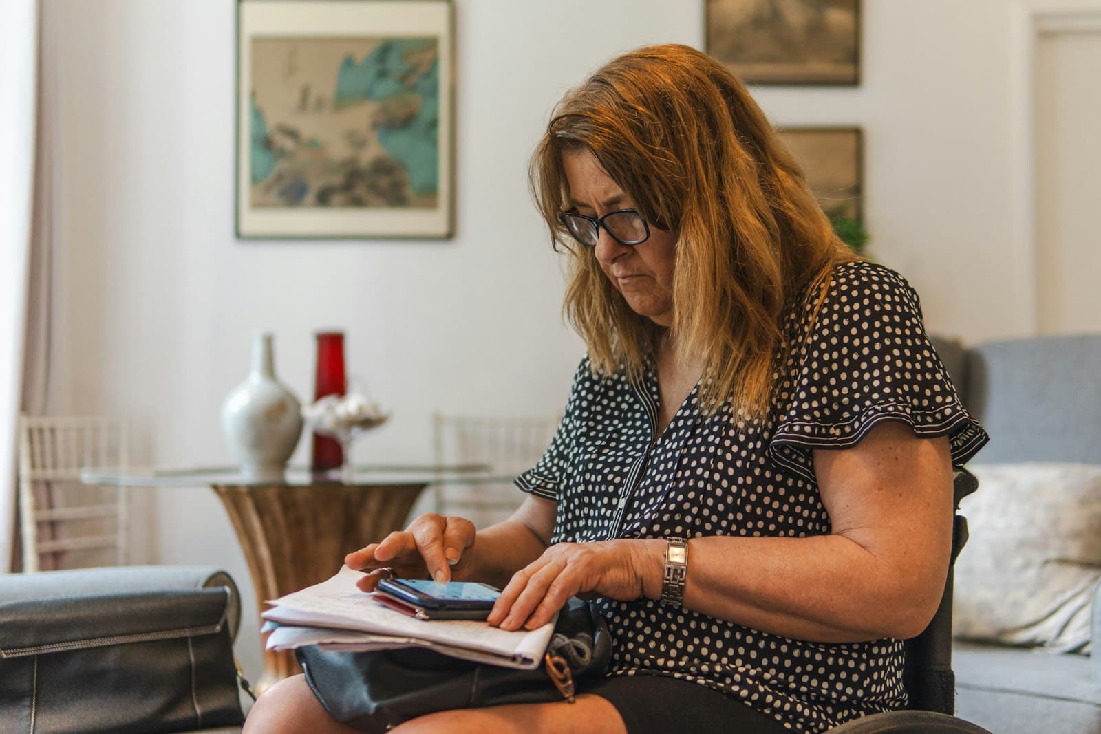 An older woman in glasses going through papers and her phone at home