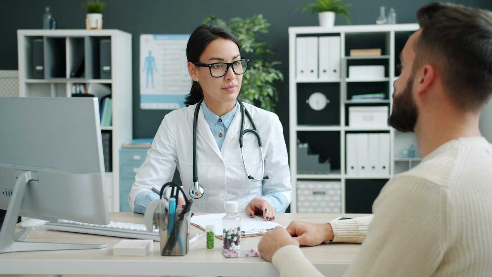A doctor in glasses listening to a male patient across her office desk