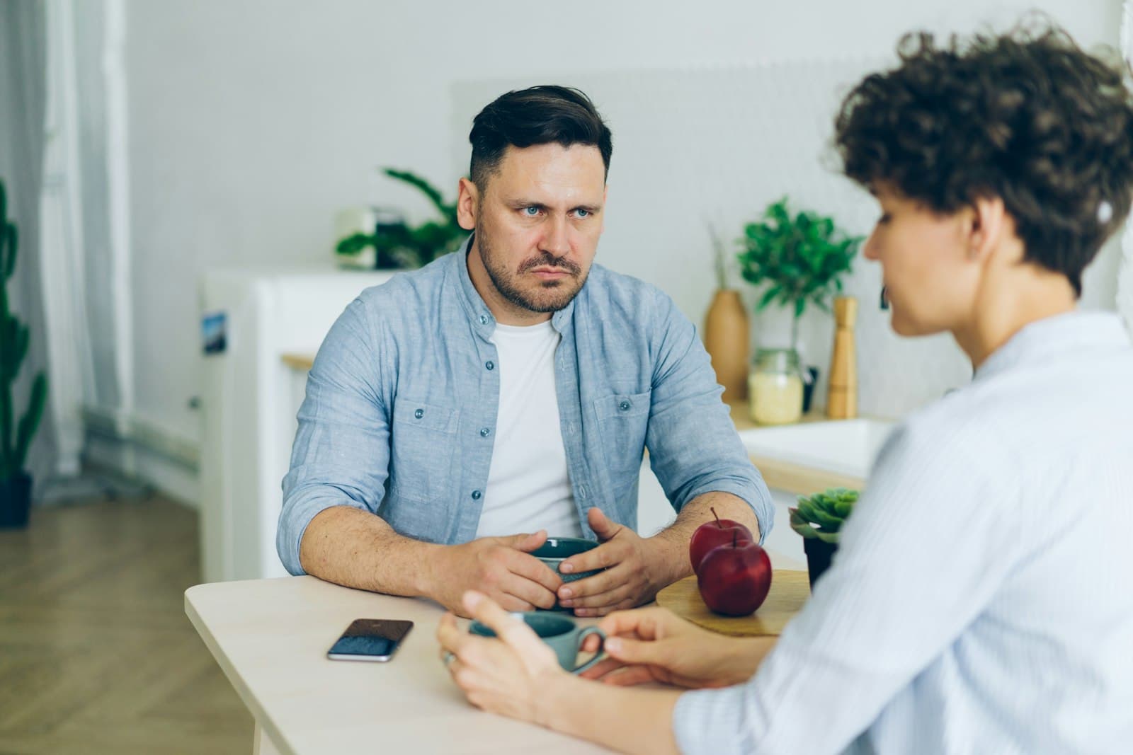 A man and a woman having a serious conversation across a small table with coffee cups