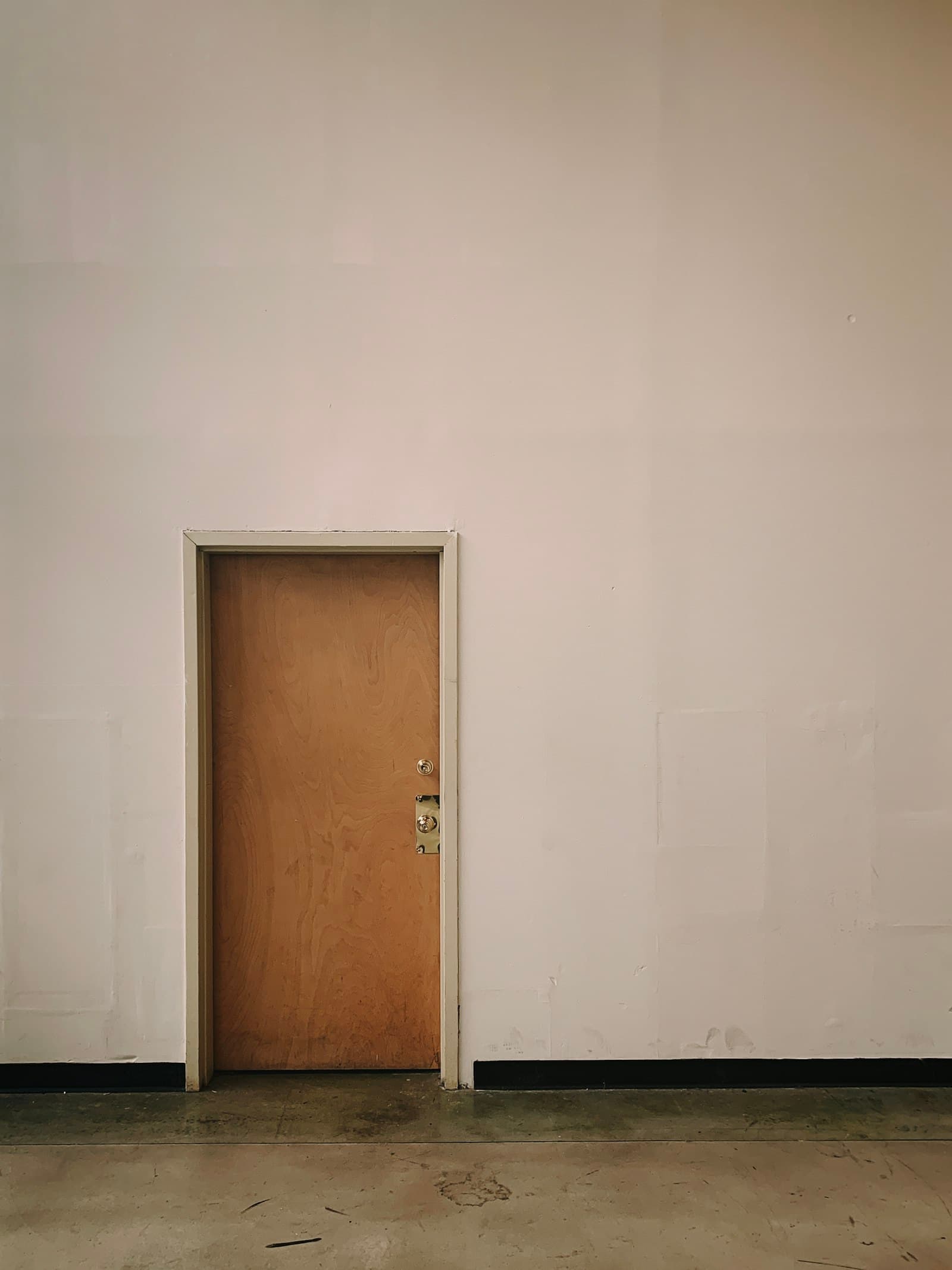A plain closed wooden door set into a bare white wall