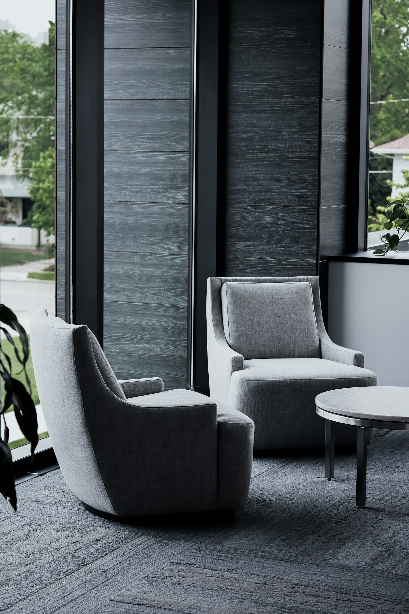 Two grey armchairs and a small table in a quiet office beside a tall window
