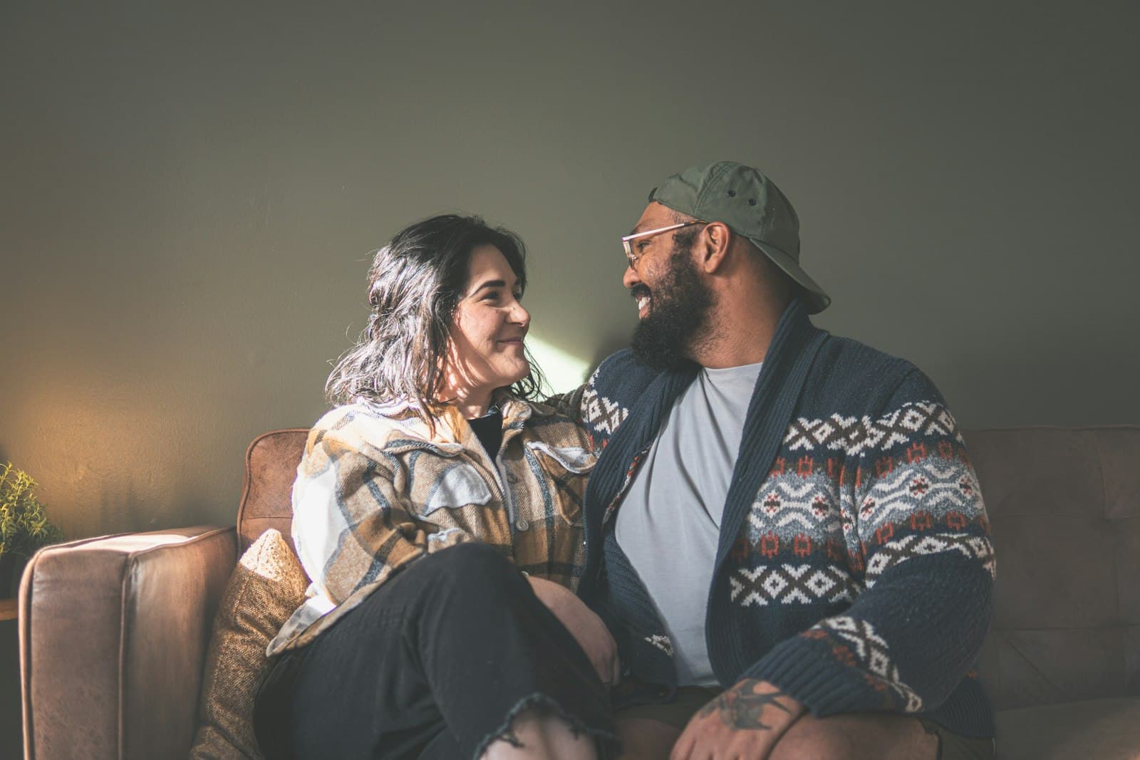 A smiling couple sitting close together on a brown sofa, turned toward each other