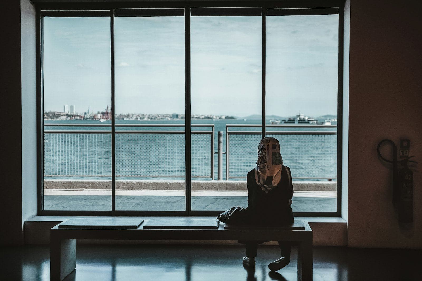 A woman standing at a tall window looking out at the water