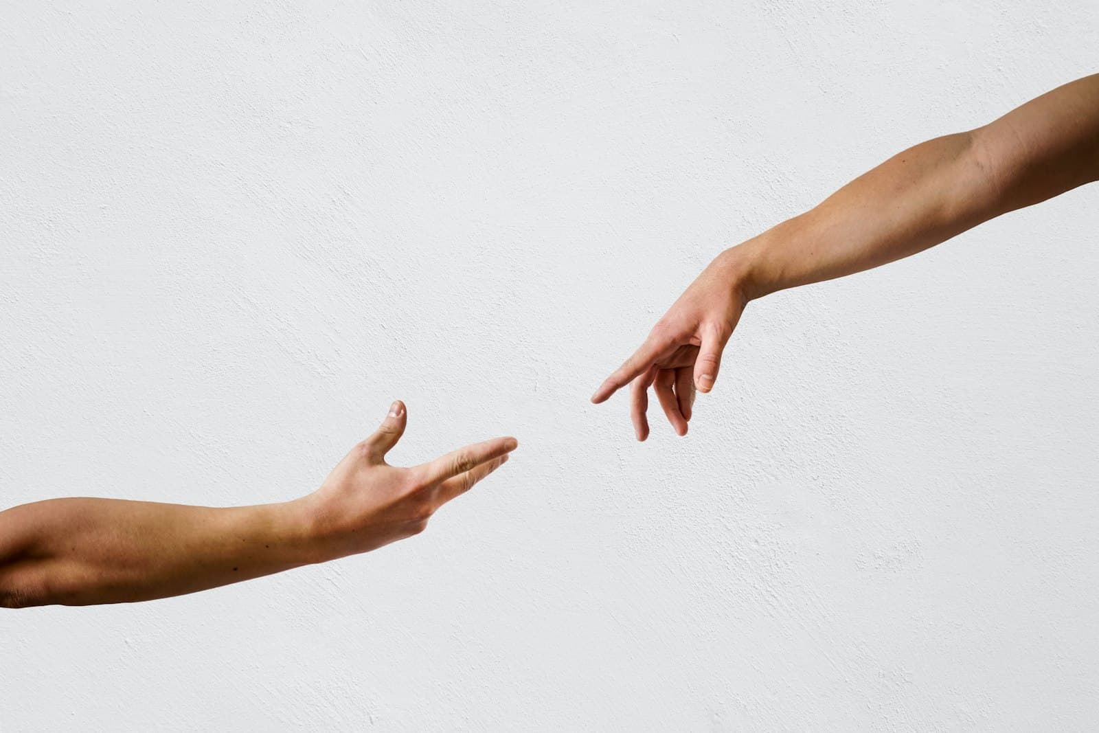 Two hands reaching gently toward each other against a pale background