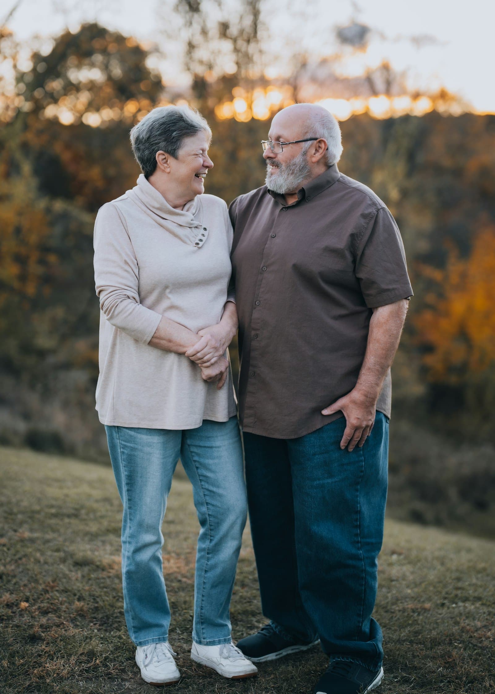 A smiling older couple standing close together on a hillside in autumn