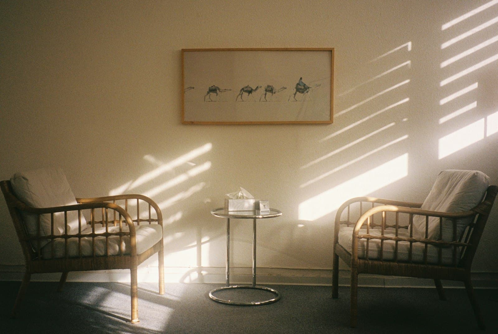 Two wooden armchairs and a small side table in a quiet room striped with sunlight