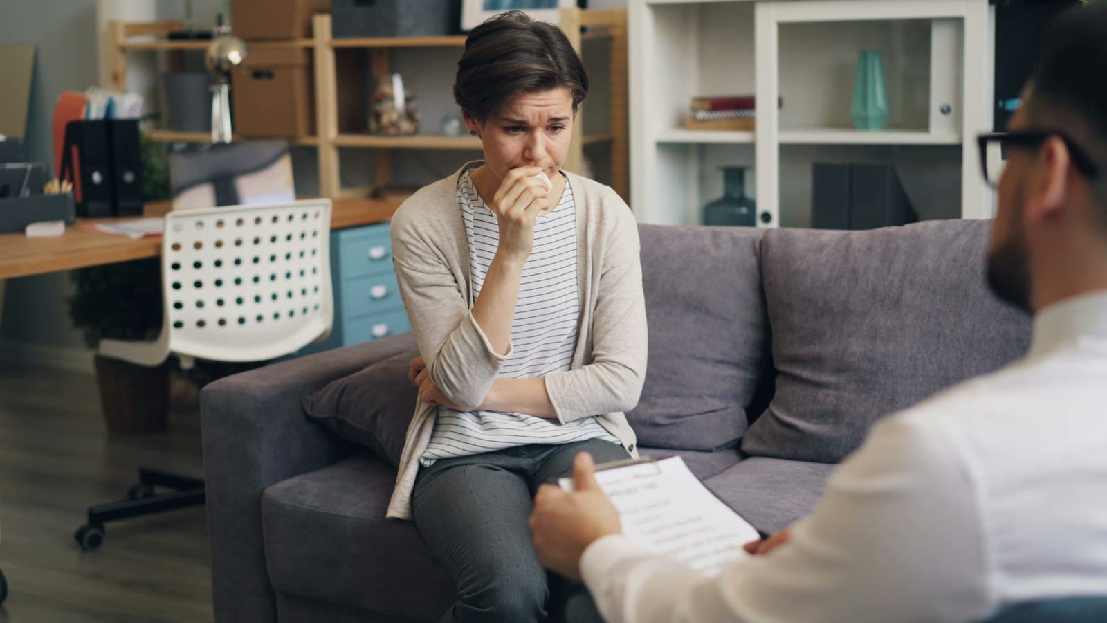 A woman holding her hand to her mouth as she speaks with a therapist taking notes
