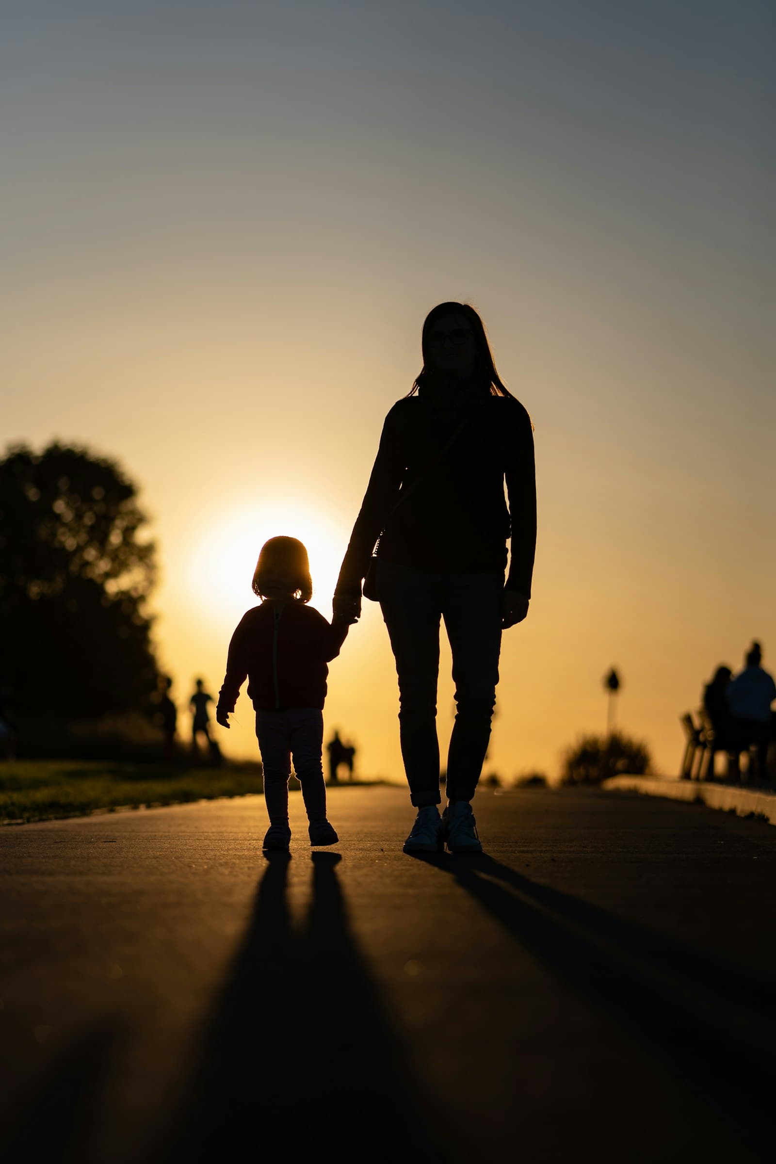 A silhouetted parent and young child walking hand in hand at sunset