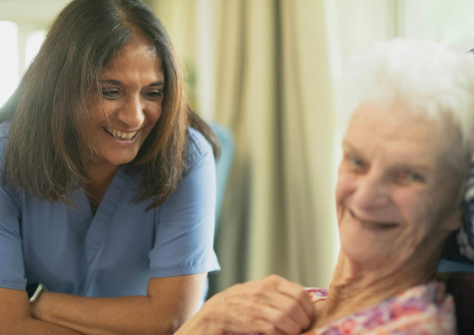 A smiling healthcare worker leaning in to talk with an elderly woman
